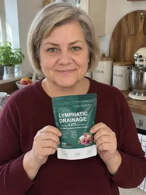 Smiling woman with short grey hair holding a pack of Zeelar softgels in her kitchen